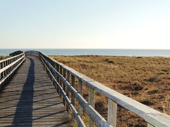 Wooden walkway leading towards sea against clear sky