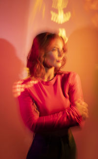 Young woman looking away with long hair and bright makeup in studio with colorful orange projector illumination