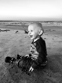 Side view of happy baby boy sitting at beach