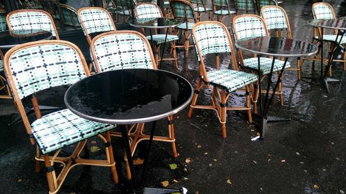 Empty chairs and tables arranged on wet sidewalk cafe