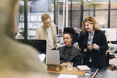 Smiling multiracial colleagues discussing over laptop while planning strategy at office