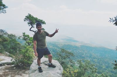 Full length of young man with arms raised on mountain against sky