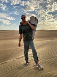 Portrait of mature woman with surfboard standing at desert against cloudy sky