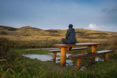 Rear view of woman sitting on field against sky