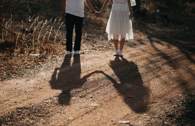 Low section of couple holding hands while standing on road