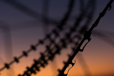 Close-up of silhouette metal fence against sky during sunset