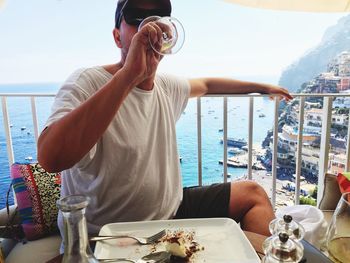 Rear view of man sitting on table at sea shore against sky