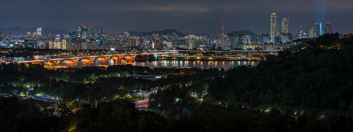 Illuminated buildings by river against sky in city at night