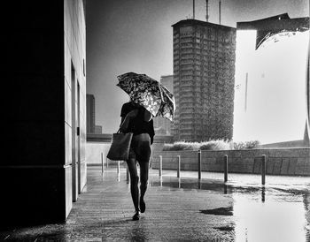 Woman walking with umbrella on wet street by buildings during monsoon