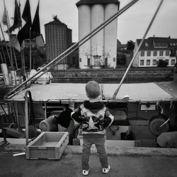 Rear view of boy standing at harbor against buildings