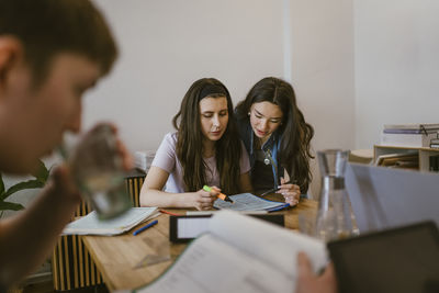 Young female friends reading while studying together at table