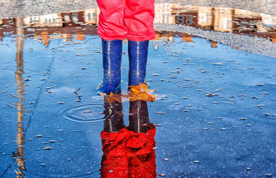 Low section of girl reflecting on puddle while standing on road during rainy season