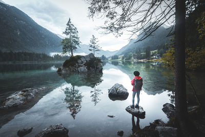 Woman standing on rock by lake against mountain