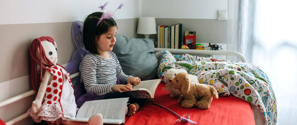 Girl in fairy costume reading book while sitting on bed at home