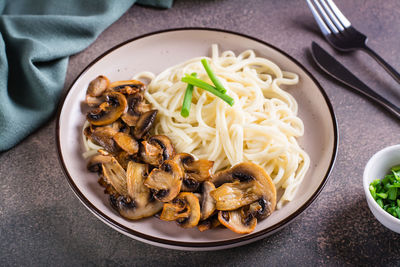 Udon noodles, fried champignons and greens on a plate on the table