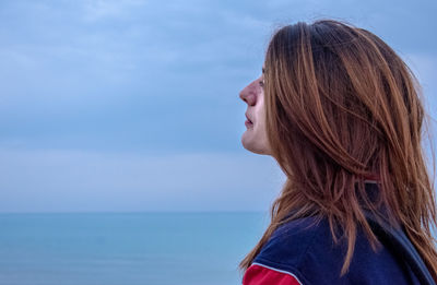 Side view of teenage girl with brown hair at beach against sky