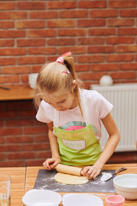 Girl rolling dough on table at home