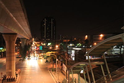 Illuminated street amidst buildings against sky at night