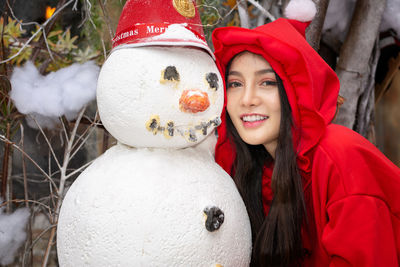 Portrait of smiling young woman by snowman