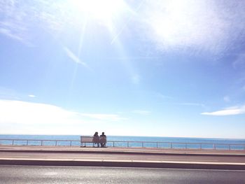 Two people sitting on bench looking out at sea