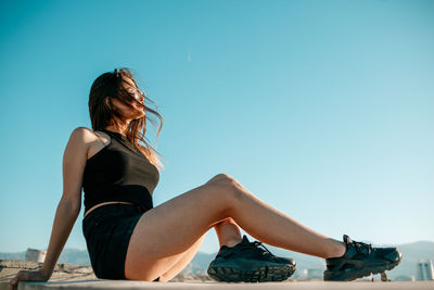 Side view of girl sitting against sky