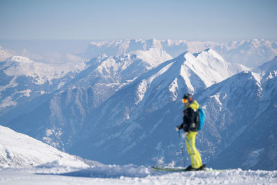 Woman hiking on snowcapped mountain peak while looking at landscape against sky