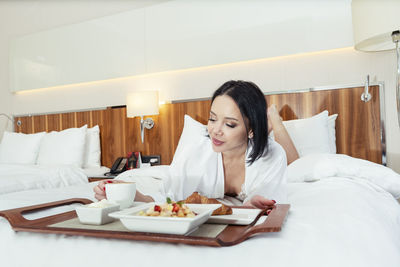 Young woman using mobile phone while sitting on bed at home