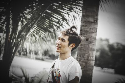 Portrait of young man standing by palm trees