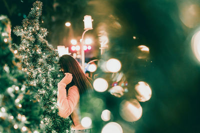 Woman by illuminated christmas tree 