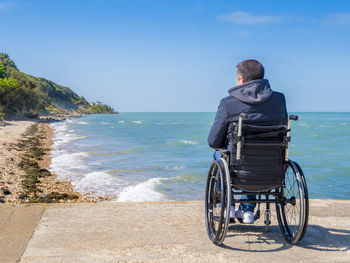 Rear view of man on wheelchair at beach against sky