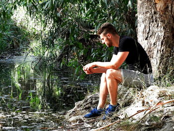 Side view of man sitting by lake in forest