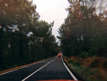 Cars on road amidst trees against sky seen through windshield