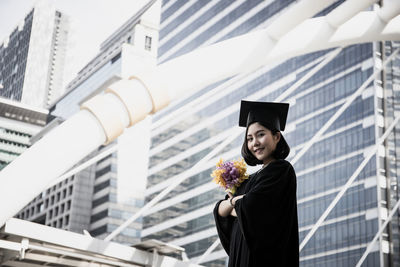 Portrait of woman wearing graduation gown while standing against building 