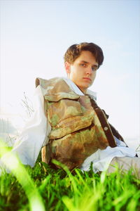 Portrait of young man sitting on grass against sky