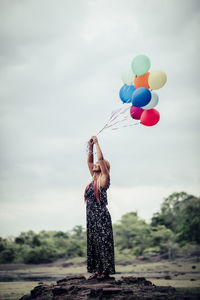 Full length of woman holding balloons while standing against sky