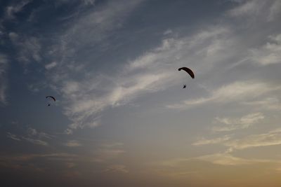 Low angle view of people paragliding against sky