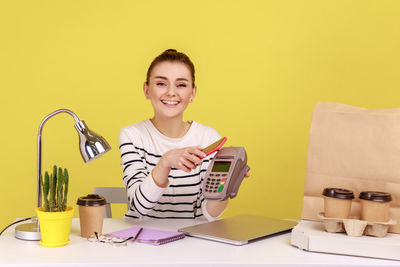 Portrait of young woman using laptop on table against yellow background