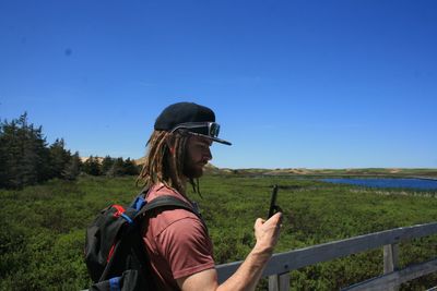 Side view of young man photographing on pier through smart phone