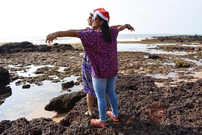 Rear view of woman on rock at beach against sky
