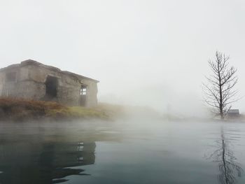 Built structure by trees against sky during foggy weather