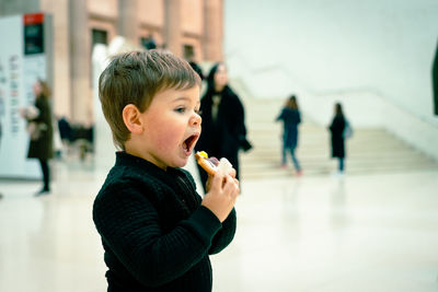 Side view of boy eating food while standing in city