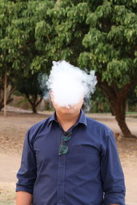 Man exhaling smoke against trees