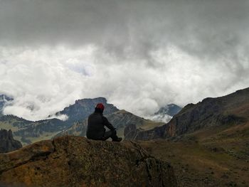 Rear view of man sitting on rock against sky