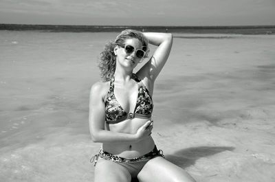 Portrait of seductive woman wearing bikini kneeling on shore at beach