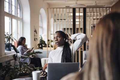 Businesswoman looking up while talking through wireless in-ear headphones at coworking office