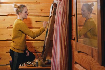 Side view of woman drawing on canvas in cottage