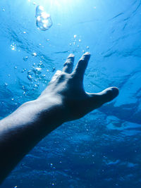 Close-up of person hand on wet blue sea