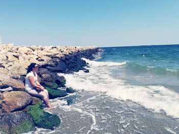 Woman on rock at beach against clear sky