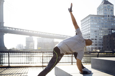 Male athlete exercising on promenade with manhattan bridge in background