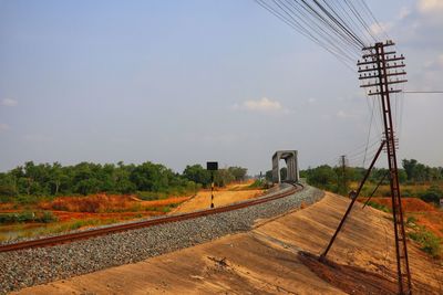 Electricity pylon by railroad tracks against sky